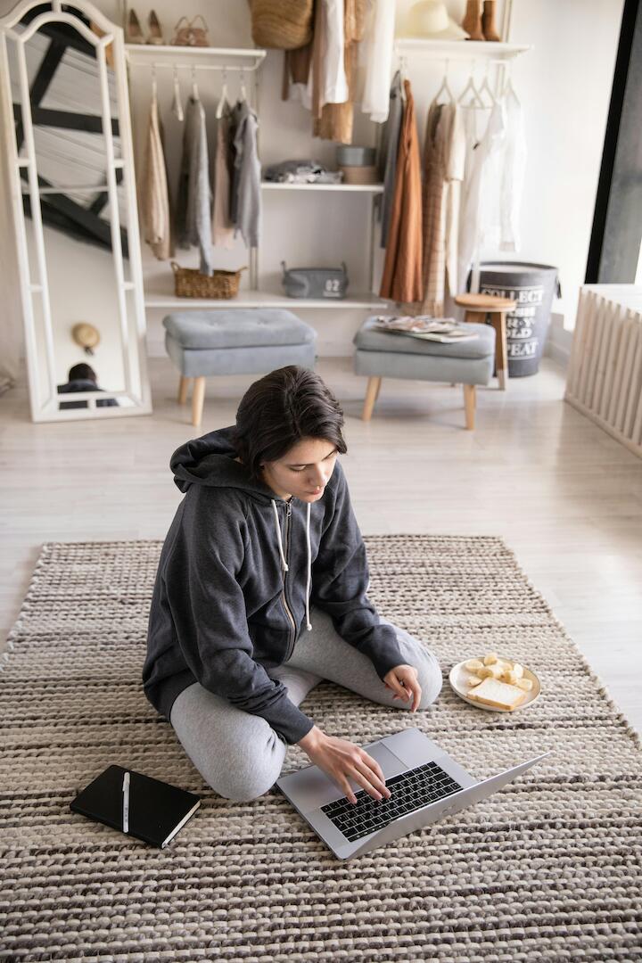 Jugendlicher sitzt auf dem Fußboden am Laptop im Hintergrund ist die Zimmereinrichtung zu sehen. Hocker, Spiegel und aufgehängte Kleidung. Jugendlicher sitzt auf dem Fußboden am Laptop im Hintergrund ist die Zimmereinrichtung zu sehen. Hocker, Spiegel und aufgehängte Kleidung.