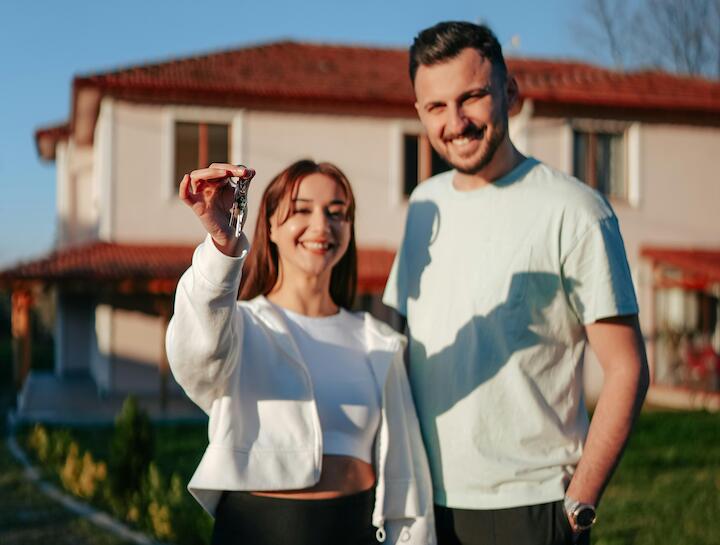 Ein junges Paar steht mit Schlüsseln in der Hand vor einem Haus