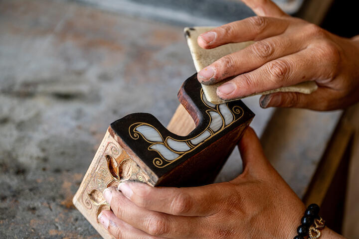 Eine Hand schleift eine mit Intarsien besetzte Kiste ab.