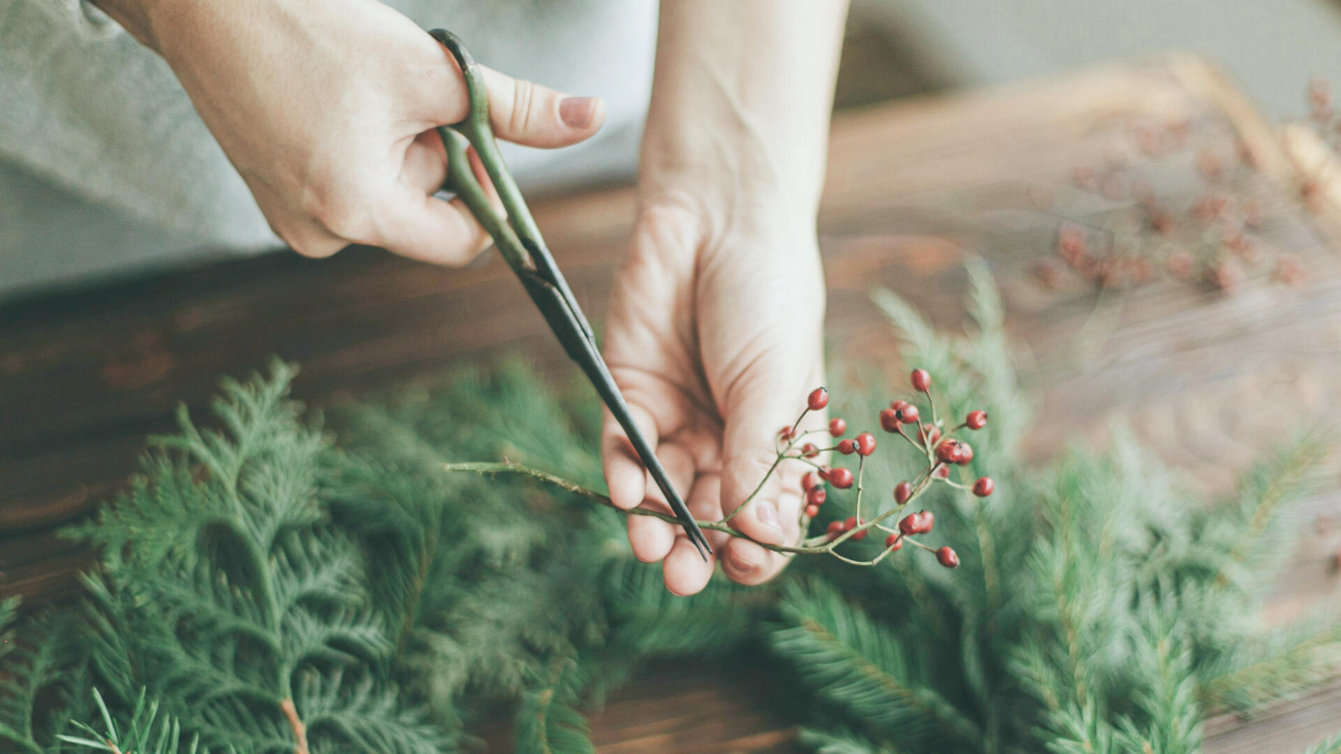 Ein Adventskranz liegt auf dem Tisch und es wird gerade Deko für ihn zurecht geschnitten