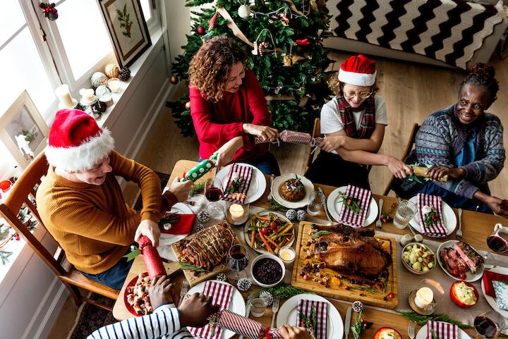 Familie und Freunde sitzen am Weihnachts-Esstisch voller Essen und reichen sich untereinander die Hände.