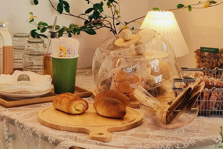 Auf einem Tisch steht eine Kanne, Gläser und es leigen dort einige Croissants. Alle leuchtet in einem warmen Licht.