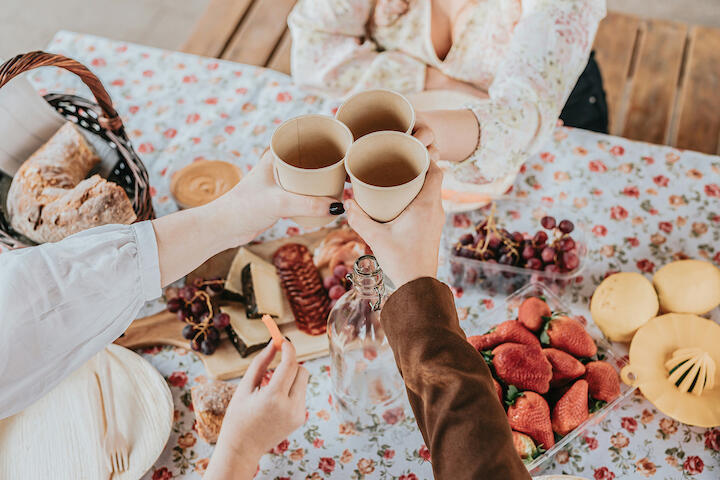 Drei Personen stoßen mit Pappbechern mit Kaffee an.