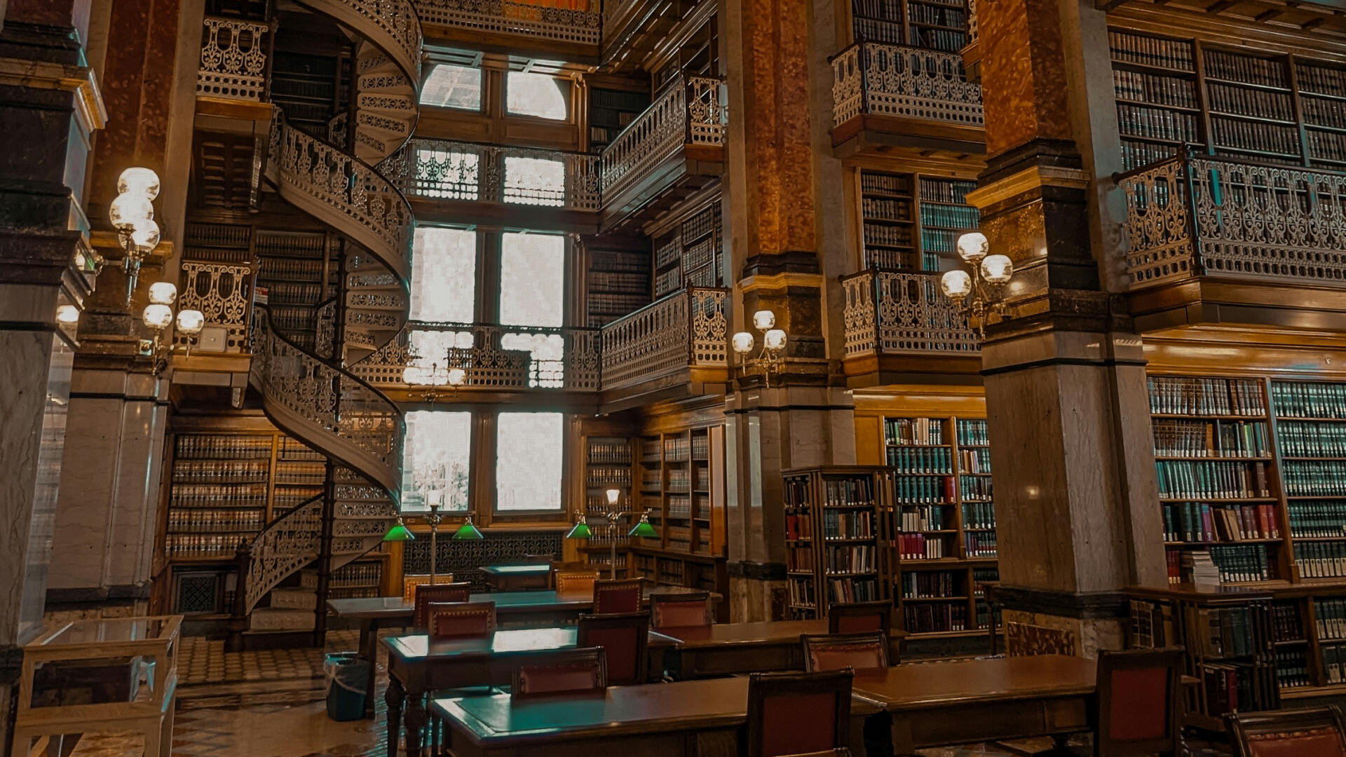 Eine Bibliothek mit hölzernen, verzierten Geländern, Büchern bis unter die Decke, schweren Tischen und ledernen Stühlen.