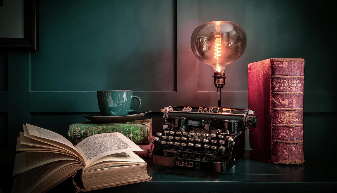 Schreibtisch mit alter Schreibmaschine, alten Büchern und einer Kaffetasse.