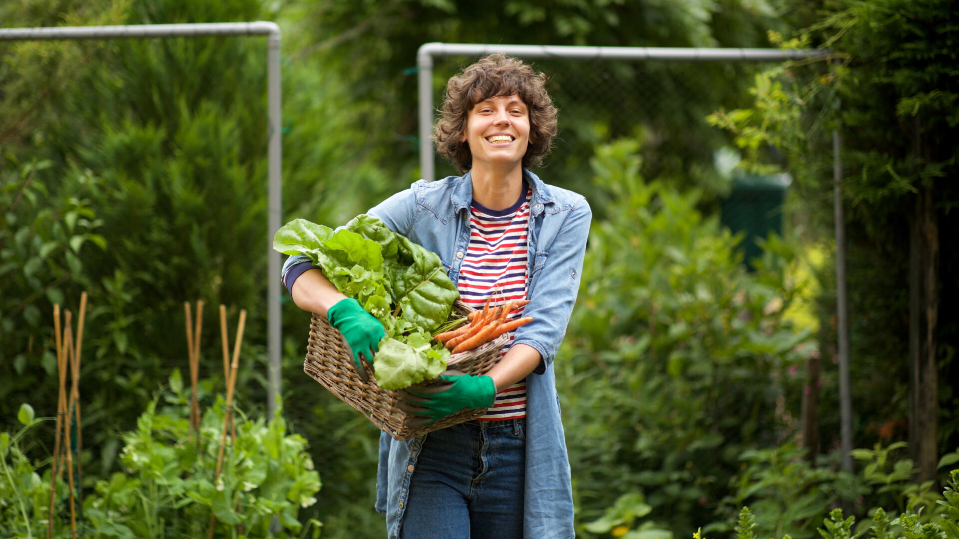 Ein junge Frau lächelt in die Kamera. Sie hält eine Kiste mit frischem Gemüse.