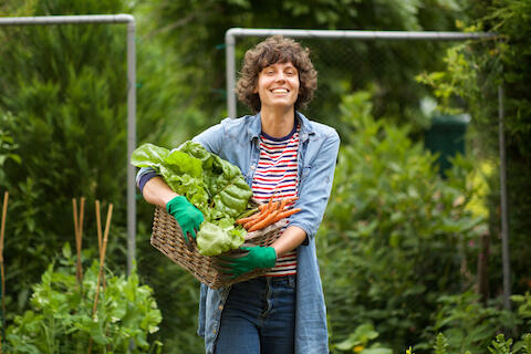 Ein junge Frau lächelt in die Kamera. Sie hält eine Kiste mit frischem Gemüse.