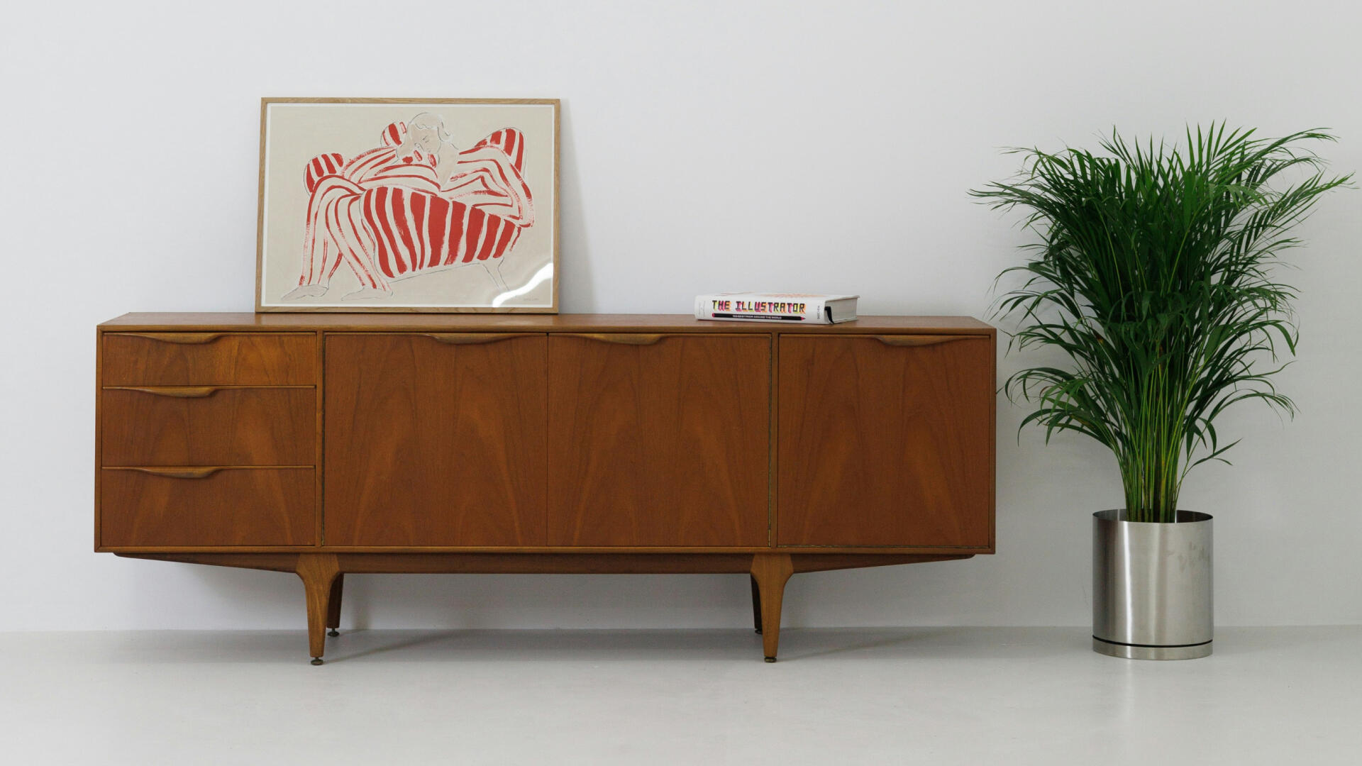 Dunkelbraune Vollholzkommode. Daneben steht eine Pflanze.