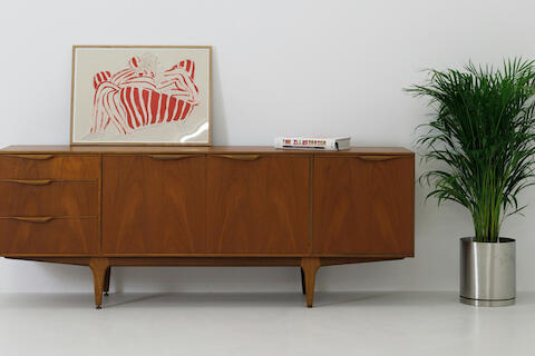 Dunkelbraune Vollholzkommode. Daneben steht eine Pflanze.