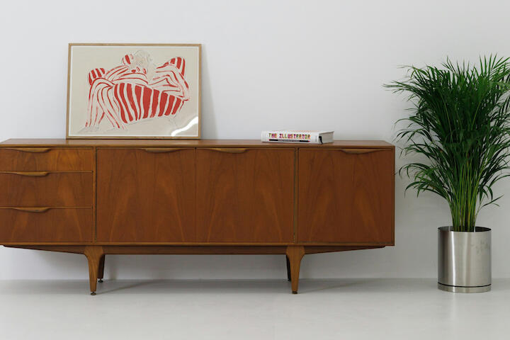 Dunkelbraune Vollholzkommode. Daneben steht eine Pflanze.