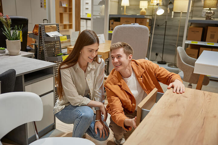 Ein junges Paar schaut sich in einem Möbelgeschäft einen Holzschreibtisch an.