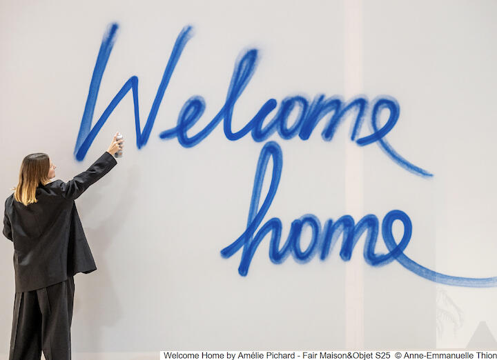 Eine Frau sprüht mit blauer Farbe die Worte: „Welcome home“