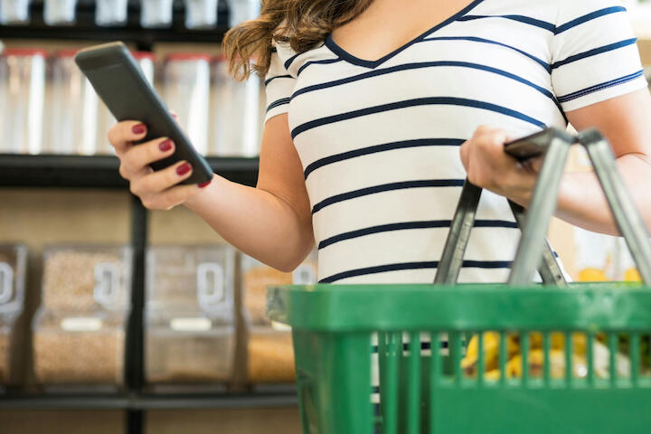 Eine Frau mit Einkaufskorb und Handy.