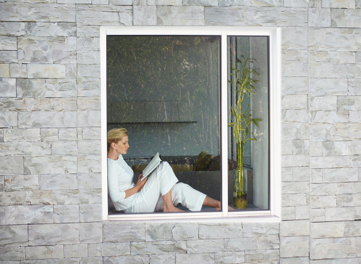 Eine Frau sitzt hinter einer Fensterfront und liest ein Buch
