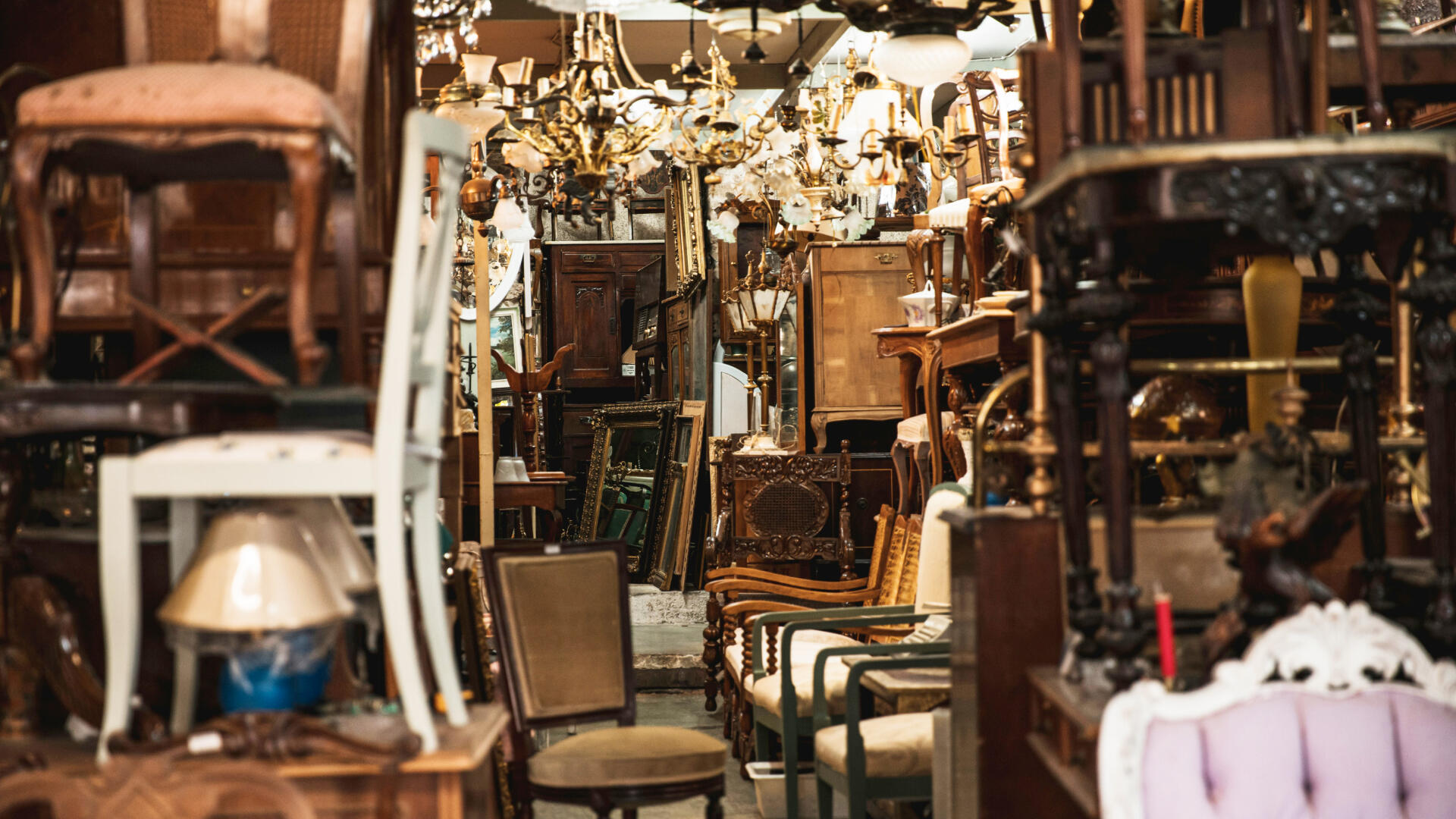 Ein Blick in eine Lagerhalle voller schöner Flohmarktfundstücke. Kornleuchter, Stühle, Spiegel etc.